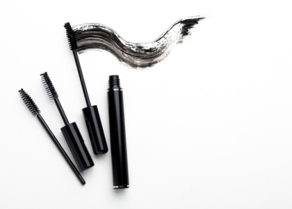 Three mascara wands lay beside an artful smear of black mascara on a white background.