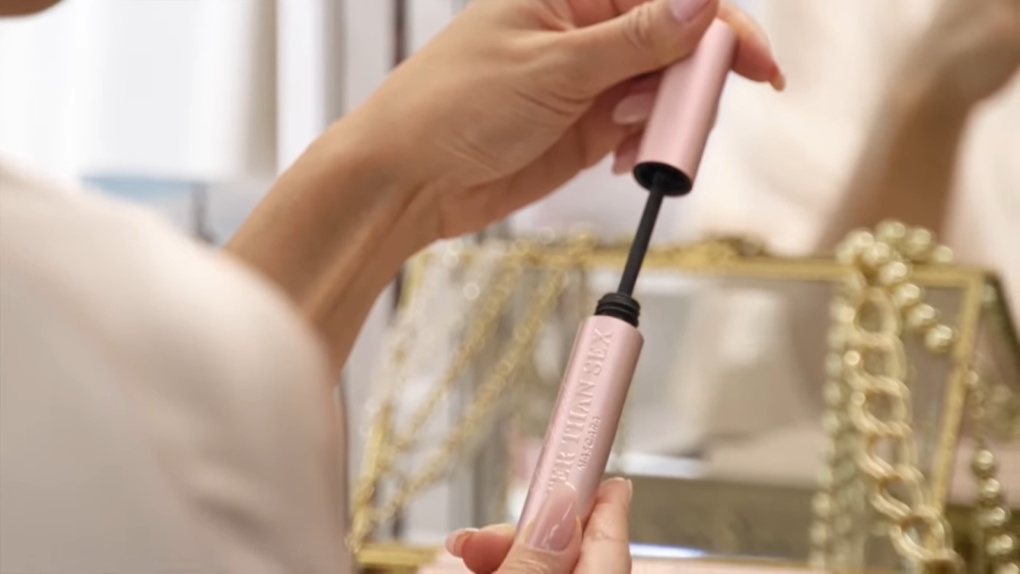 woman holds a pink mascara in front of the blurred mirror and transparent box